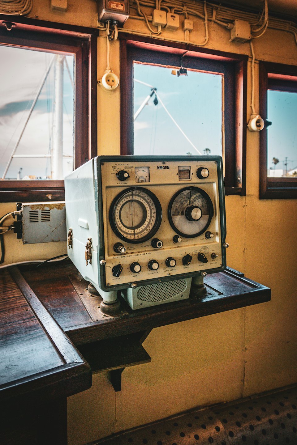 Marine radio direction finder with dials on a wooden shelf inside a boat.