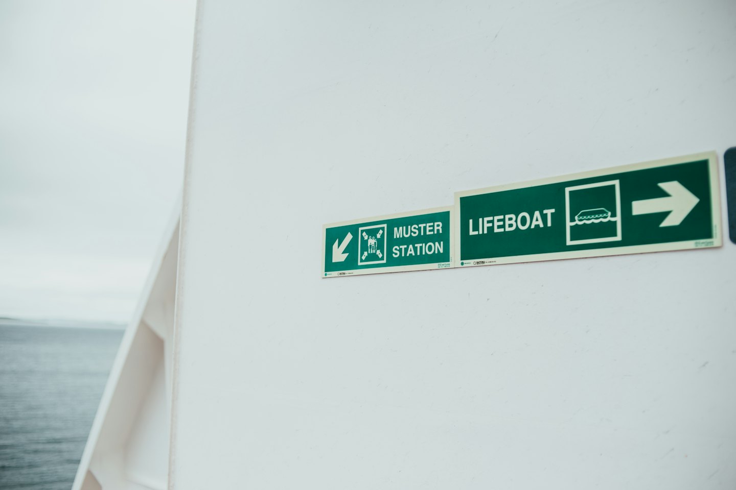 Muster station and lifeboat safety sign on a ship wall.