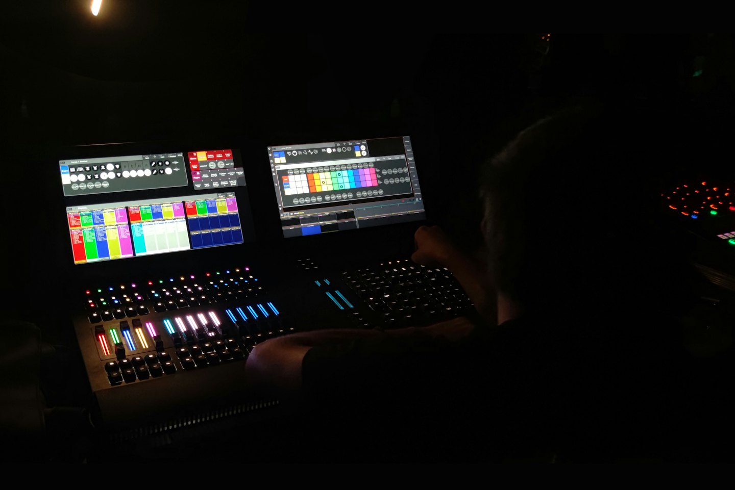 Technician adjusts soundboard with colorful glowing buttons and screens.