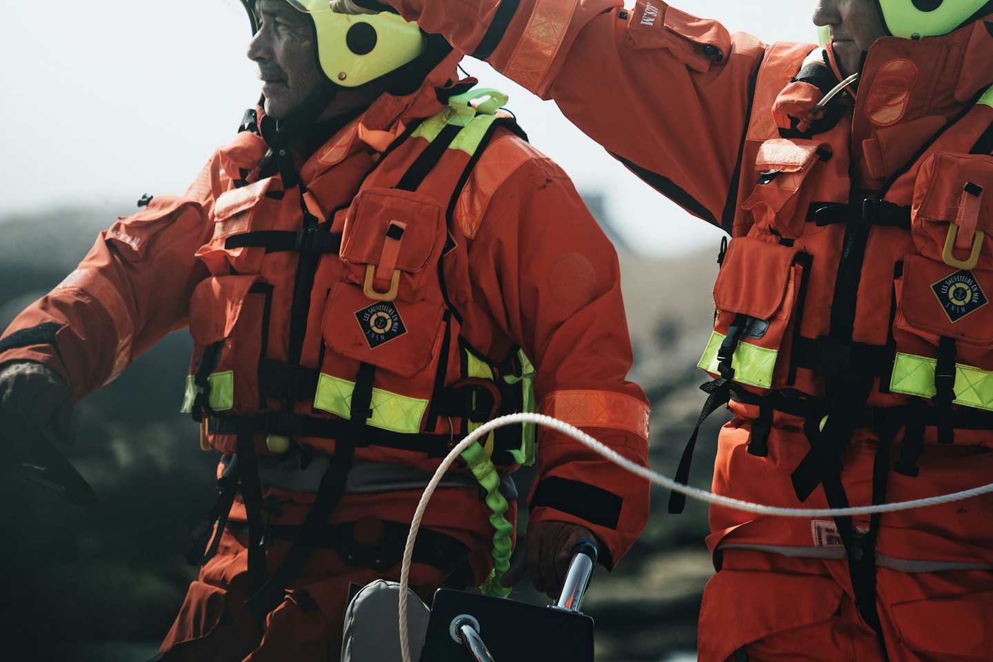 Two rescue professionals wearing orange dry suits work on a boat.